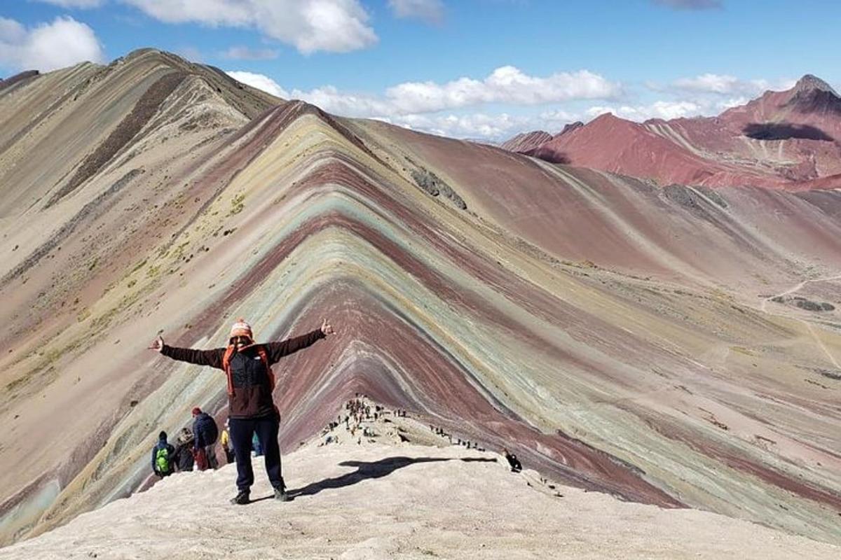 Ein Mann steht mit ausgestreckten Armen auf einem Berggipfel