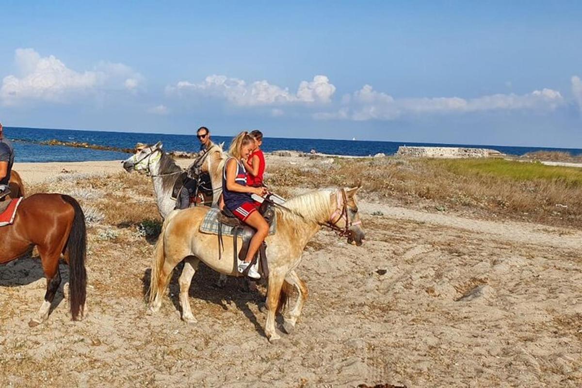 een groep mensen die op paarden op het strand rijden