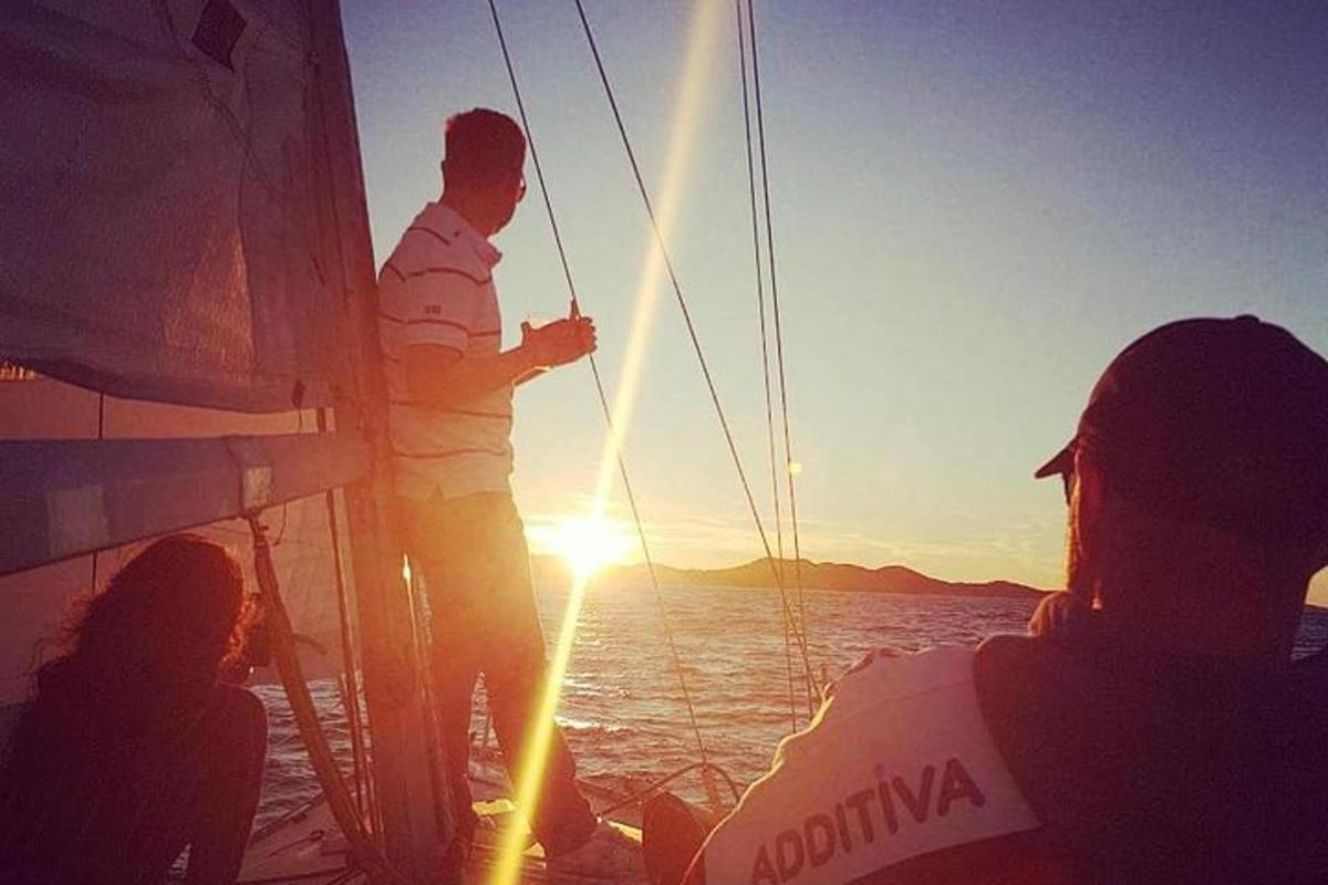 a man standing on the side of a boat at sunset