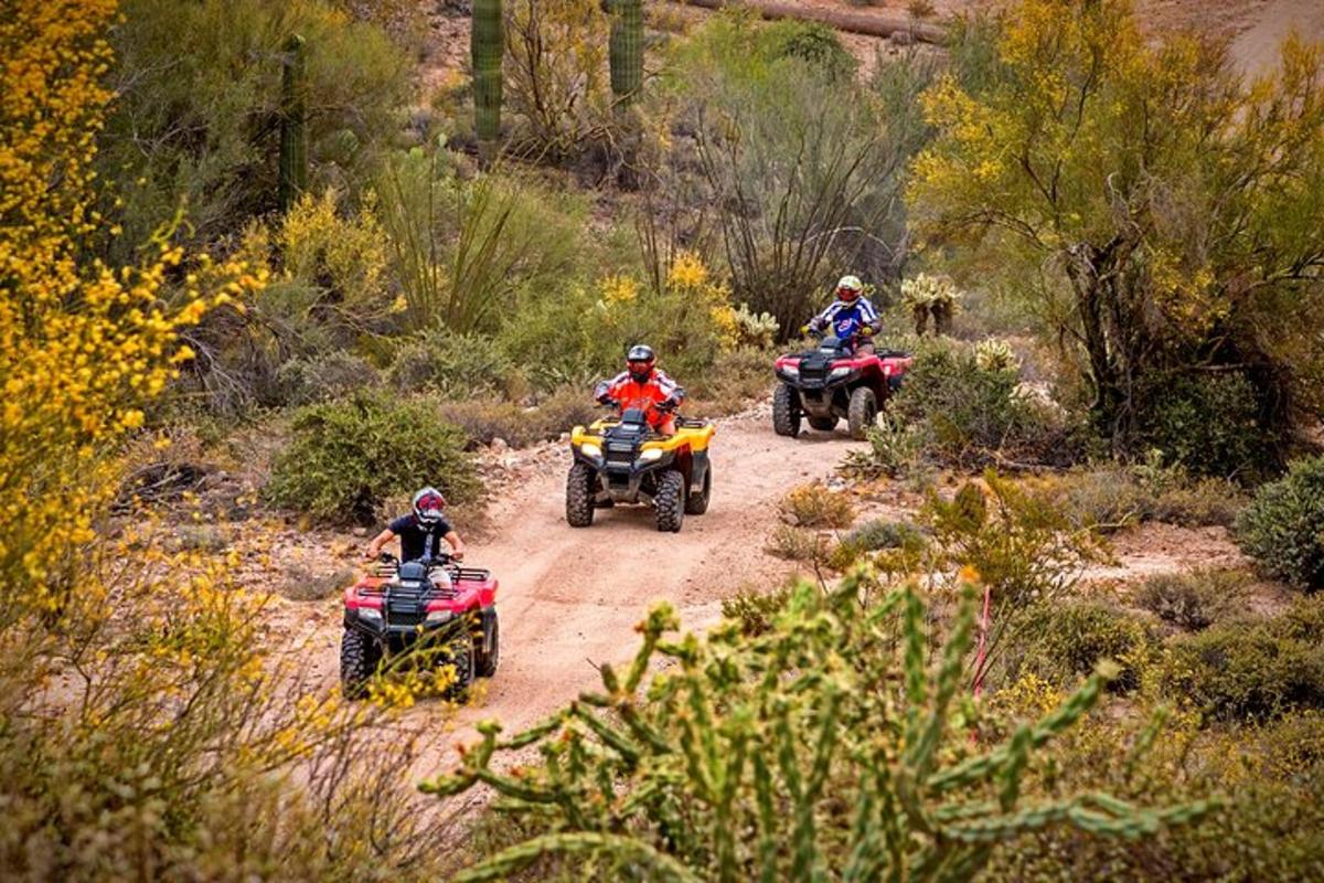 three people riding on atvs on a dirt road