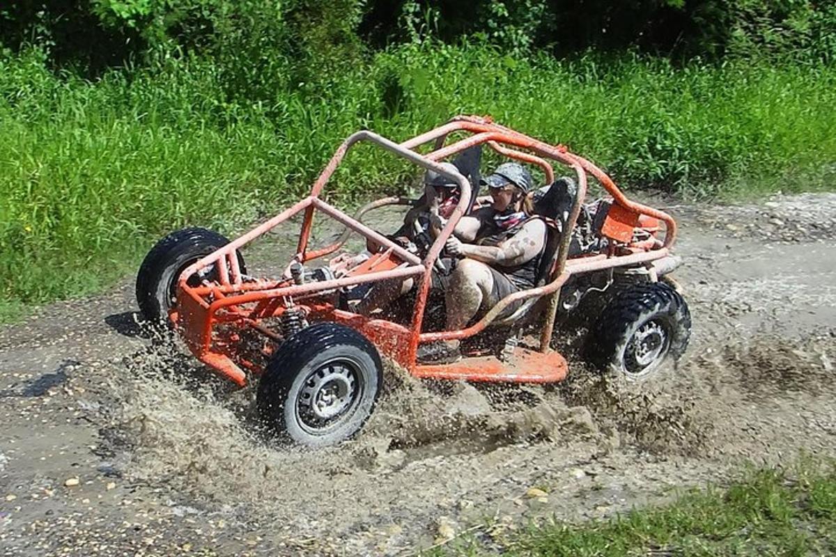 two people riding in an orange four wheeler in the mud