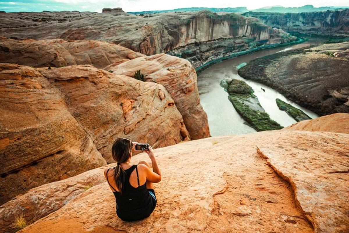 a woman sitting on a rock taking a picture of a river