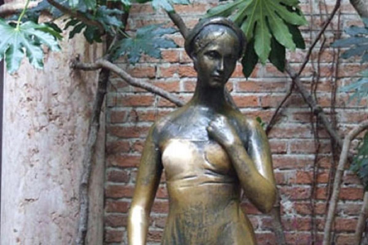 a bronze statue of a woman standing next to a brick wall