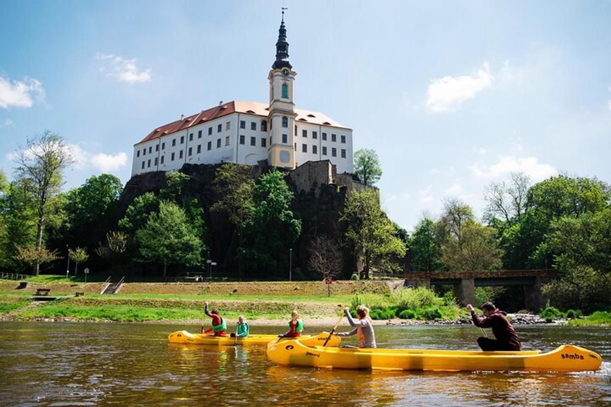 Skupina lidí v kánoích na řece s hradem