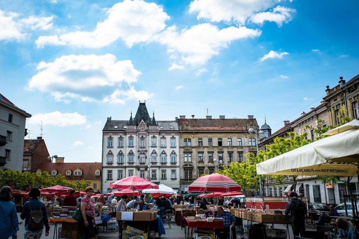 a market with tables and red umbrellas in front of a building