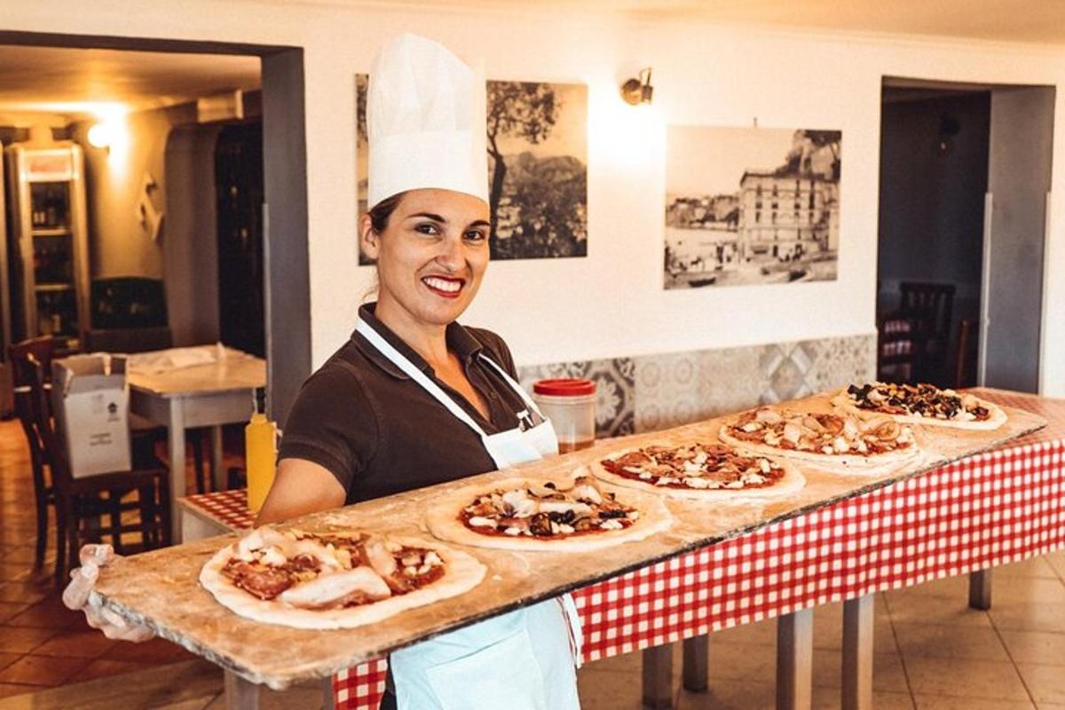 Kona í kokkabúningi heldur á afgreiðsluborði með pizzum