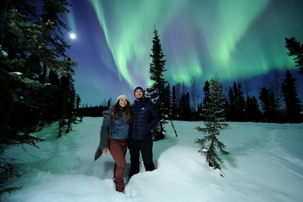 a man and a woman standing in the snow under the aurora