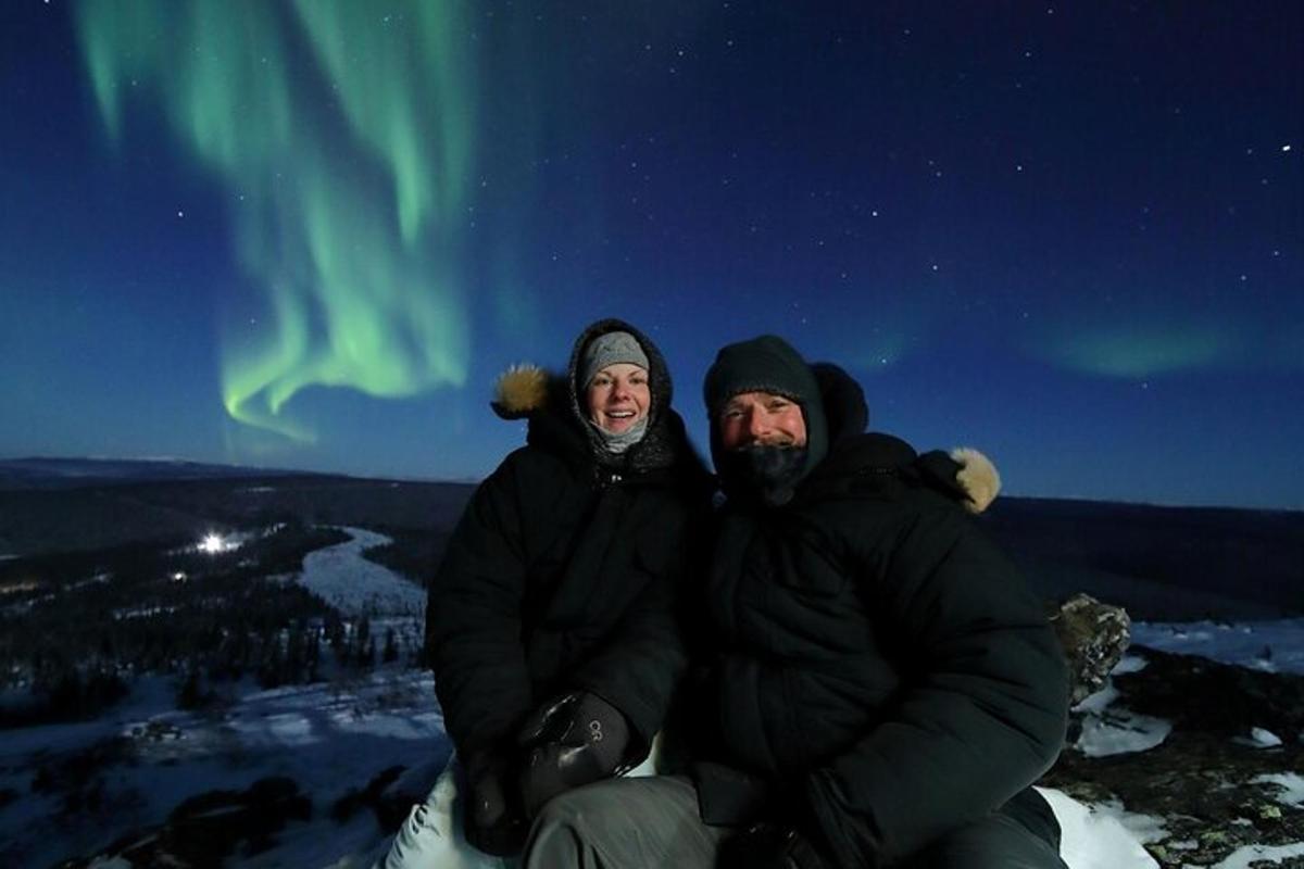 two people sitting on top of a mountain under the northern lights