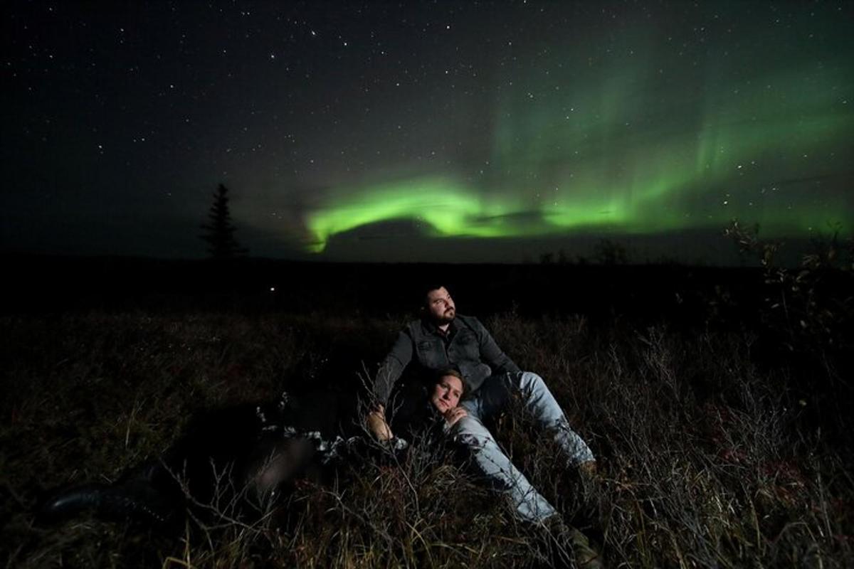 duas pessoas deitadas em um campo sob a aurora boreal