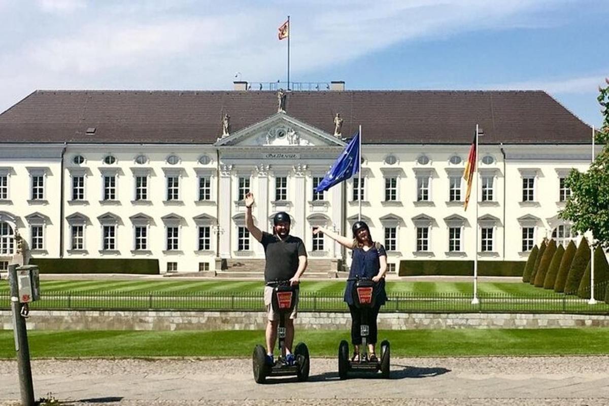 um homem e uma mulher andando de segway em frente a um prédio branco