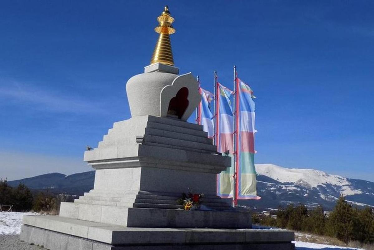 sebuah monumen dengan bendera di hadapan gunung