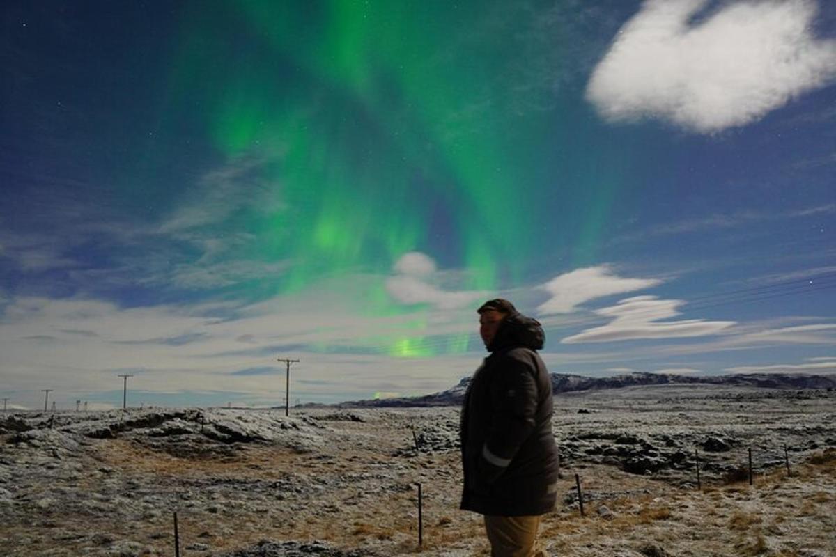 un home està dret en un camp sota l'aurora boreal