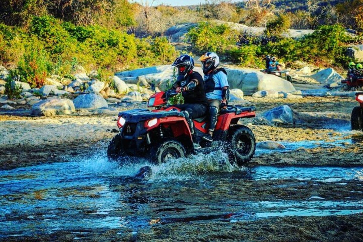 Dos personas viajando en un vehículo de cuatro ruedas a través de un río