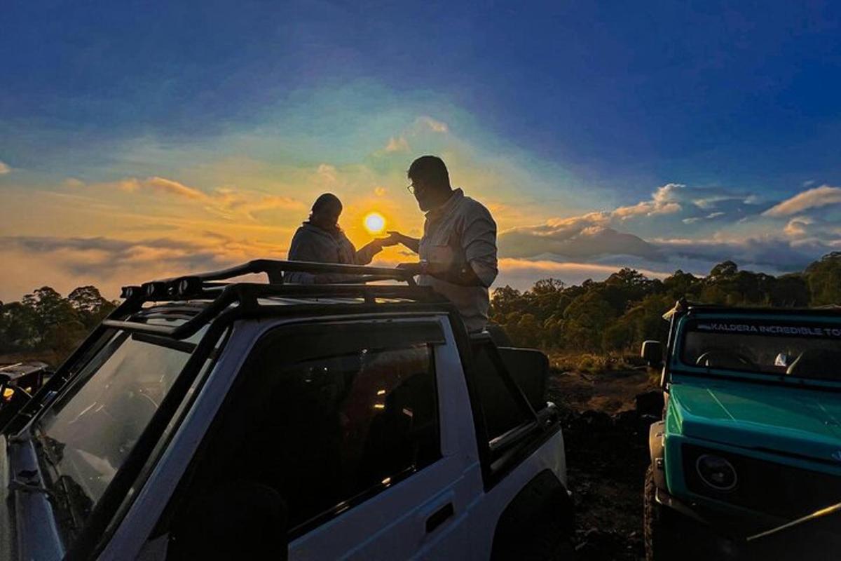 two men standing on the roof of a jeep at sunset