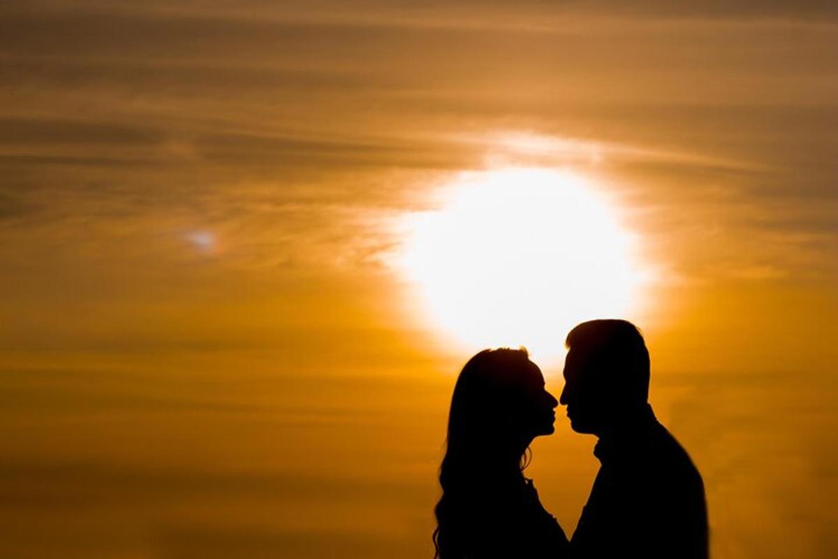 a silhouette of a couple kissing in front of the sun