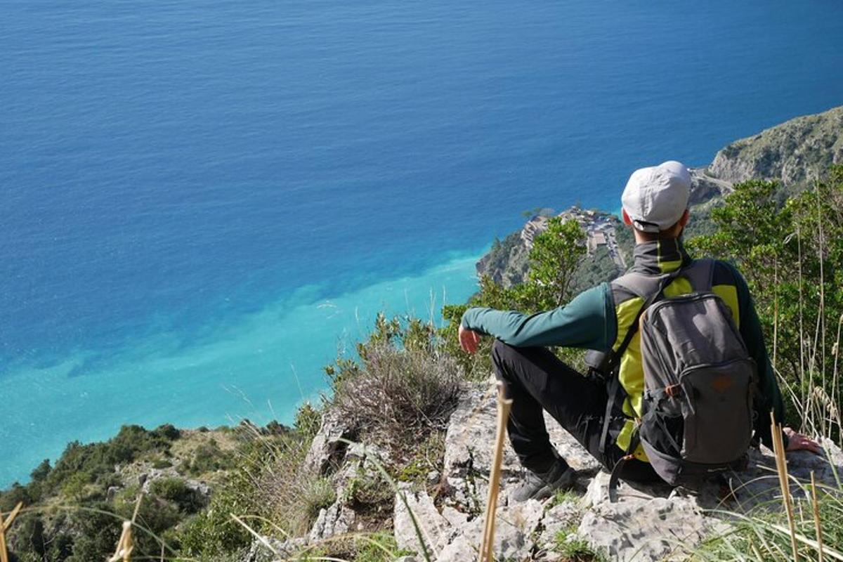 una persona con uno zaino seduta su una scogliera che guarda l'oceano