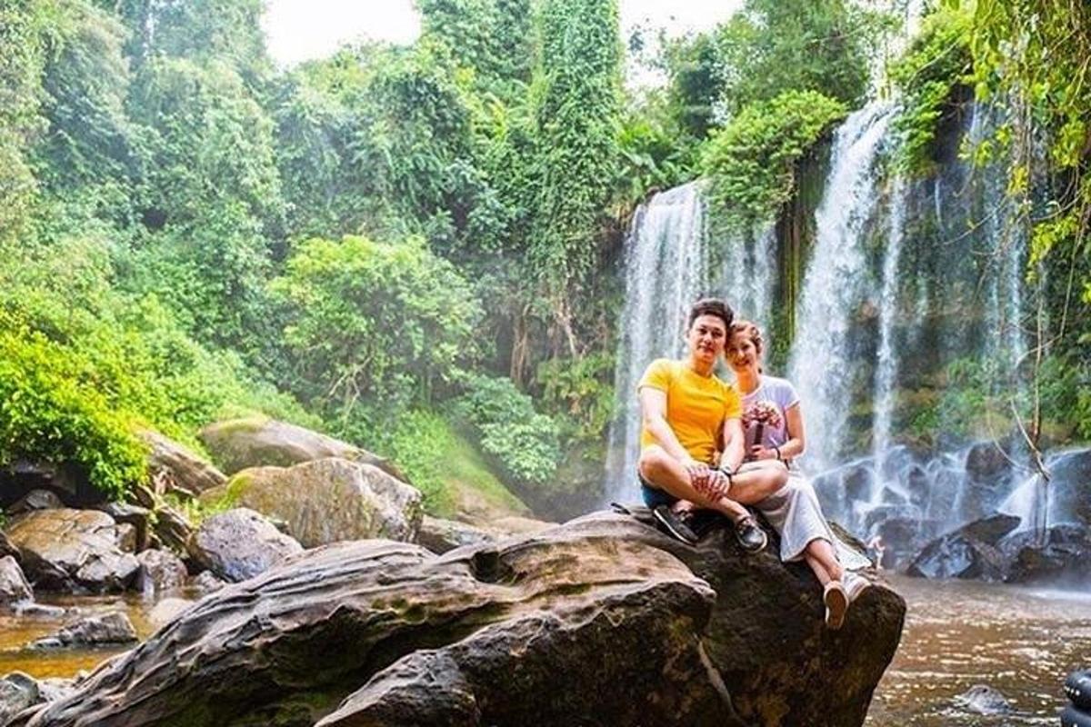 Ein Mann und eine Frau sitzen auf einem Felsen vor einem Wasserfall