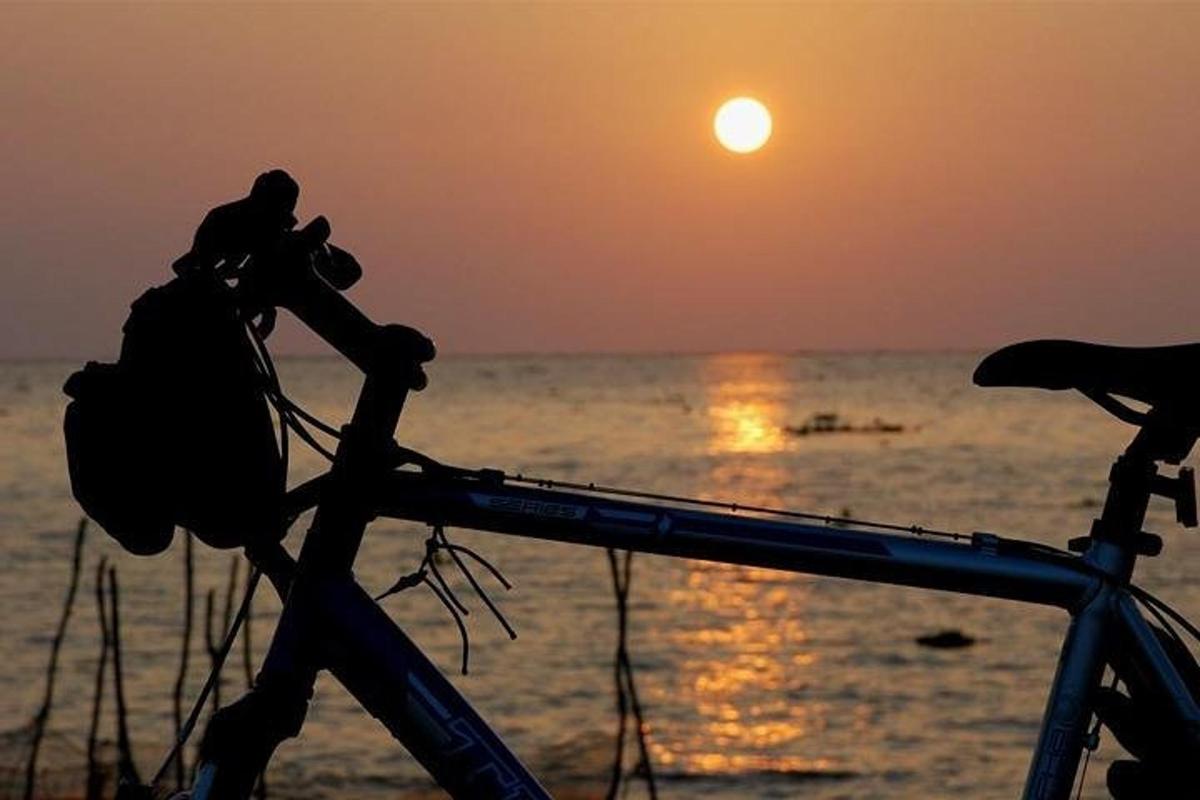 eine Person, die bei Sonnenuntergang auf einem Fahrrad am Strand sitzt
