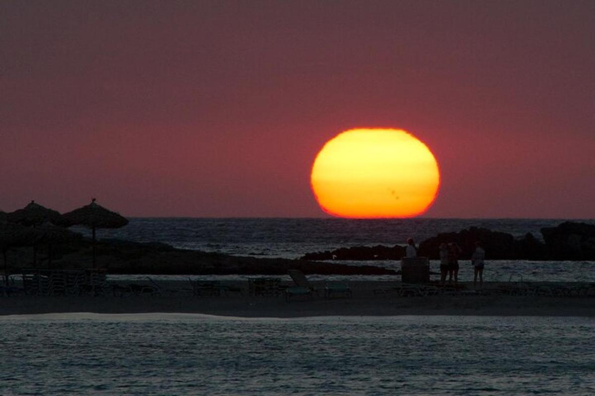 Západ slunce nad oceánem s lidmi stojícími na pláži
