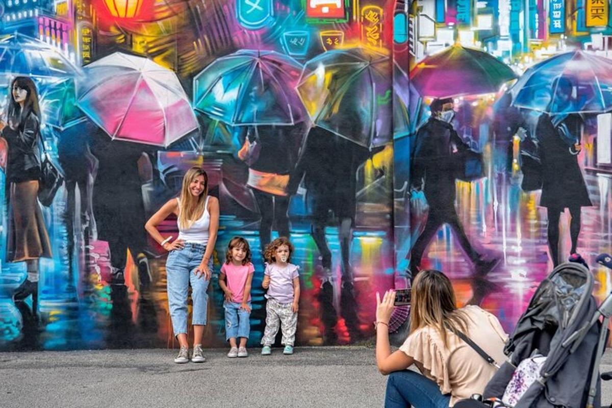 eine Frau und zwei Kinder stehen mit Regenschirmen vor einer Mauer