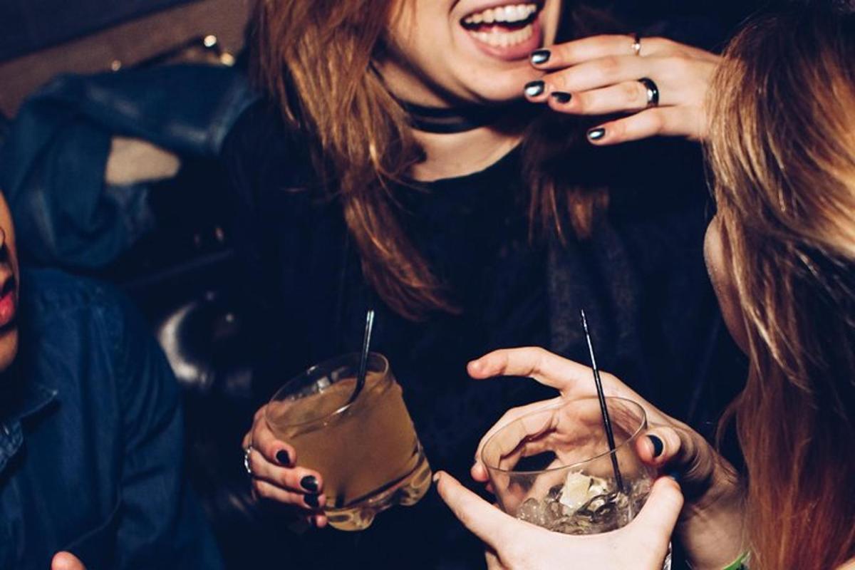 dua wanita tertawa sambil memegang minuman di tangan mereka