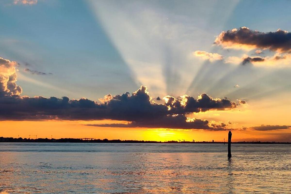 una posta de sol sobre l'aigua amb un pal a l'aigua