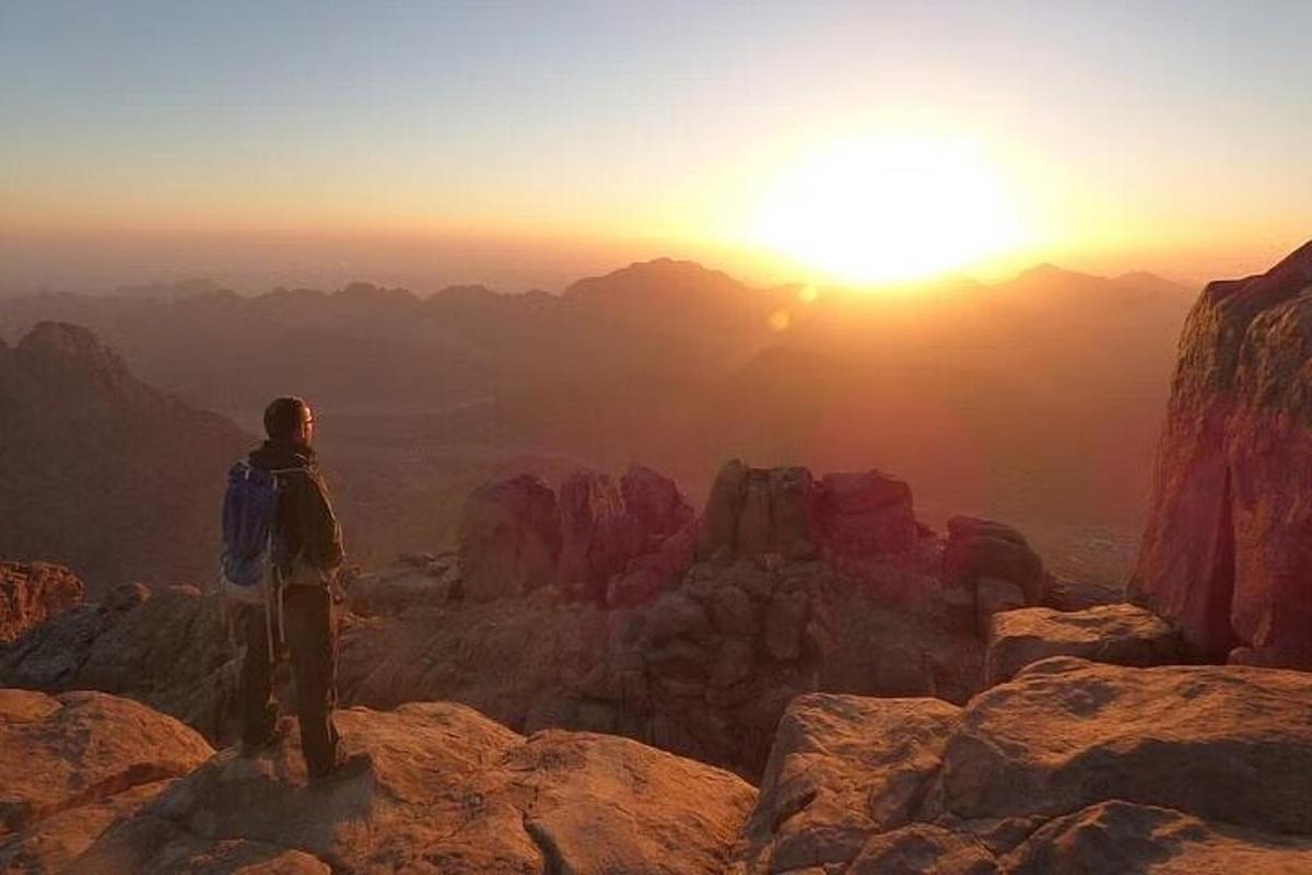 شخص يقف على قمة جبل يشاهد غروب الشمس