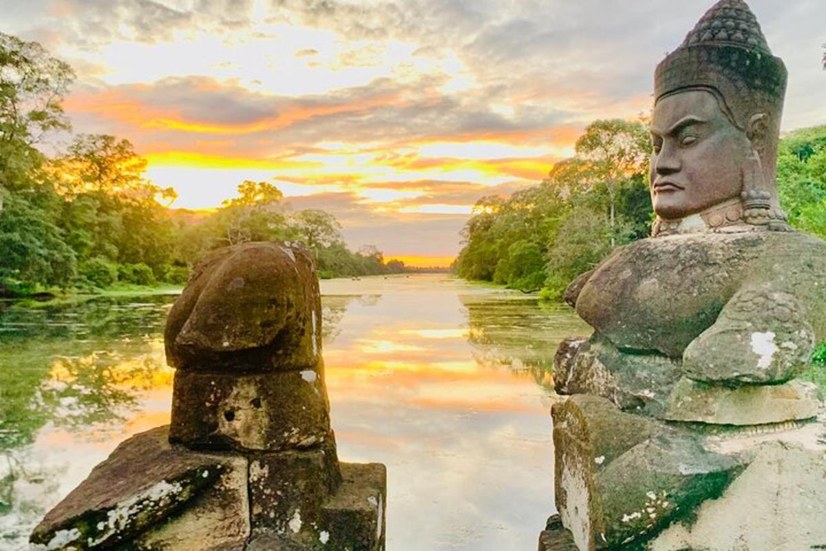 duas estátuas em pé ao lado de um rio ao pôr do sol