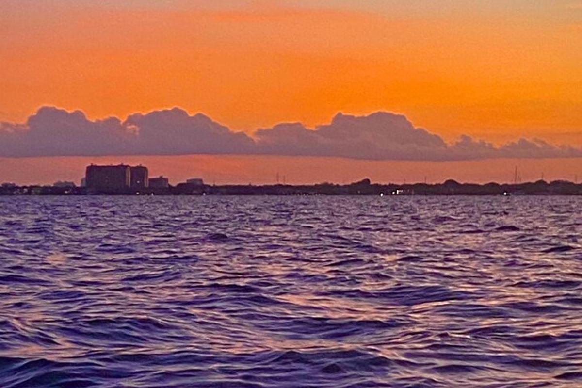 isang paglubog ng araw sa ibabaw ng tubig na may isang lungsod sa background