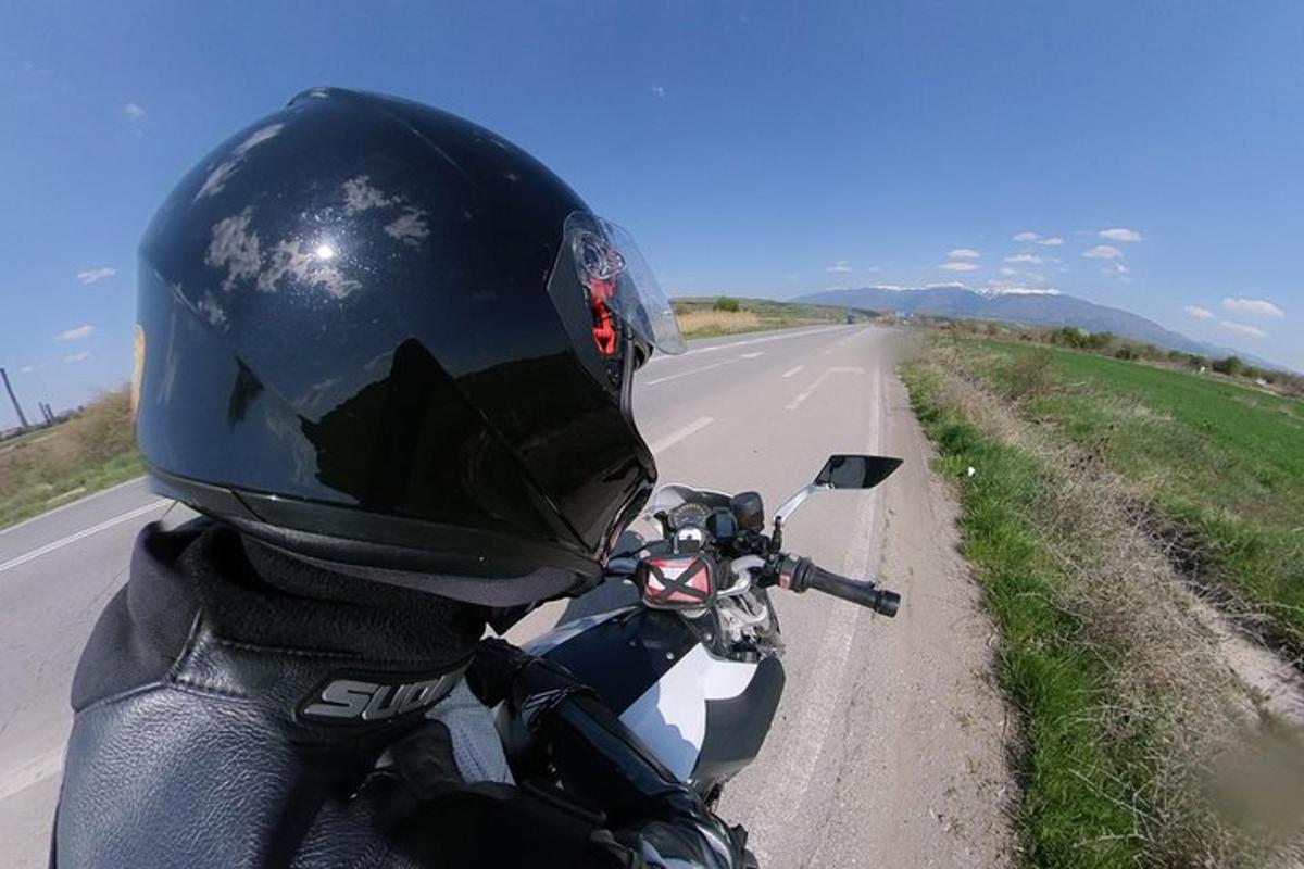 oseba, ki nosi čelado in vozi motorno kolo po cesti