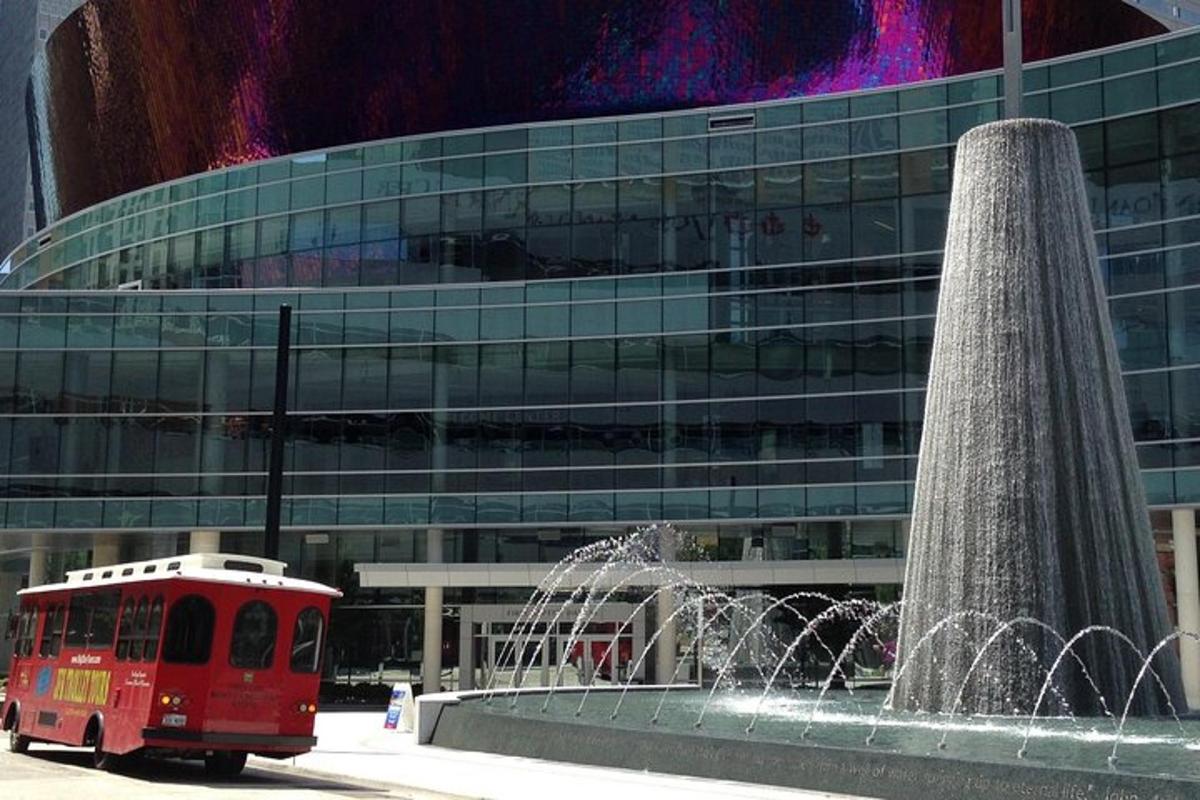 a red bus in front of a building with a fountain
