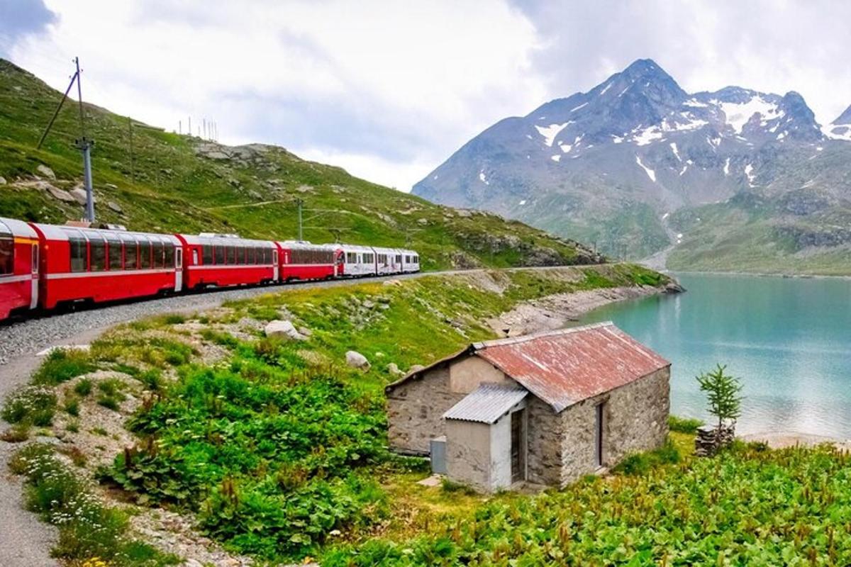 Ein roter Zug fährt einen Hügel neben einem See hinunter