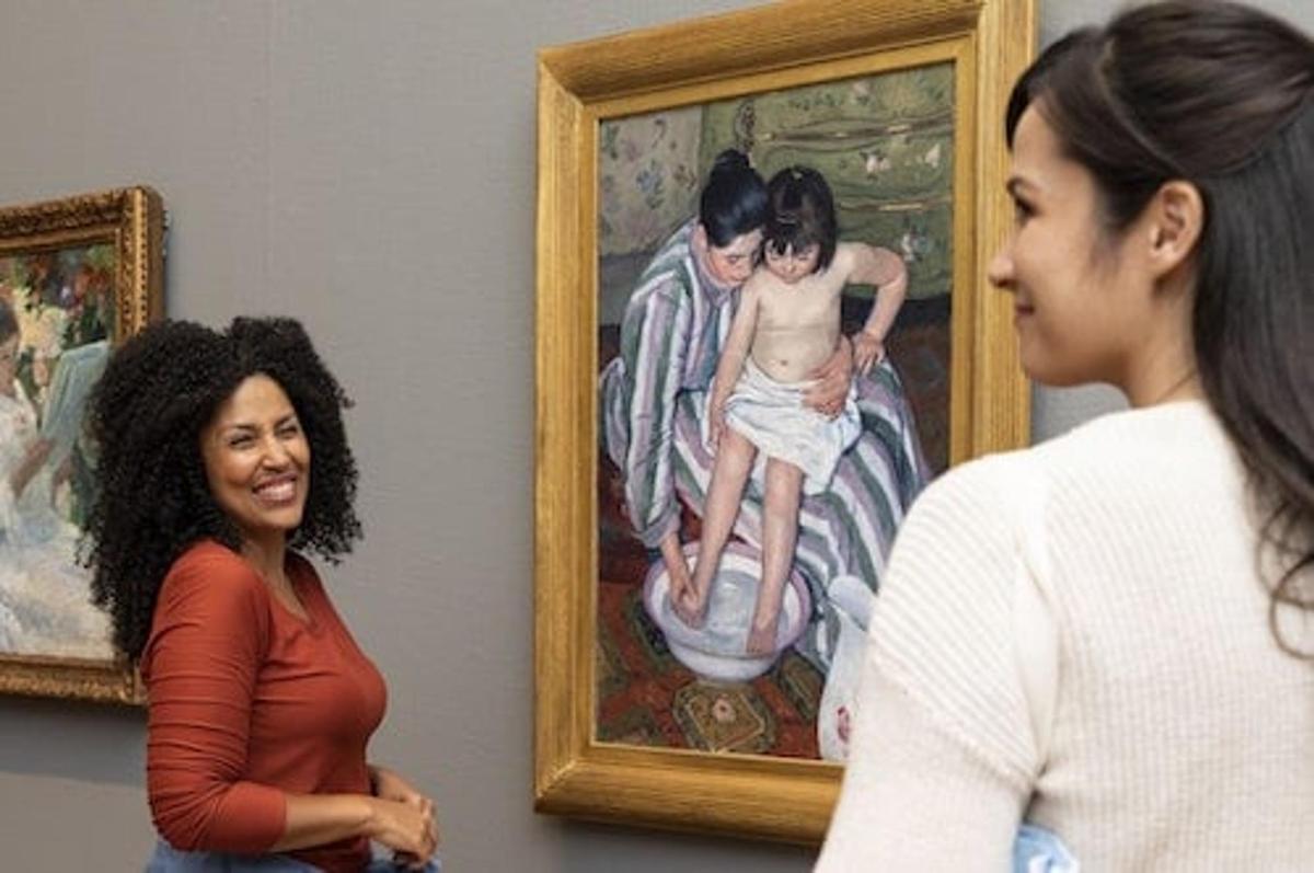 two women standing in front of a painting