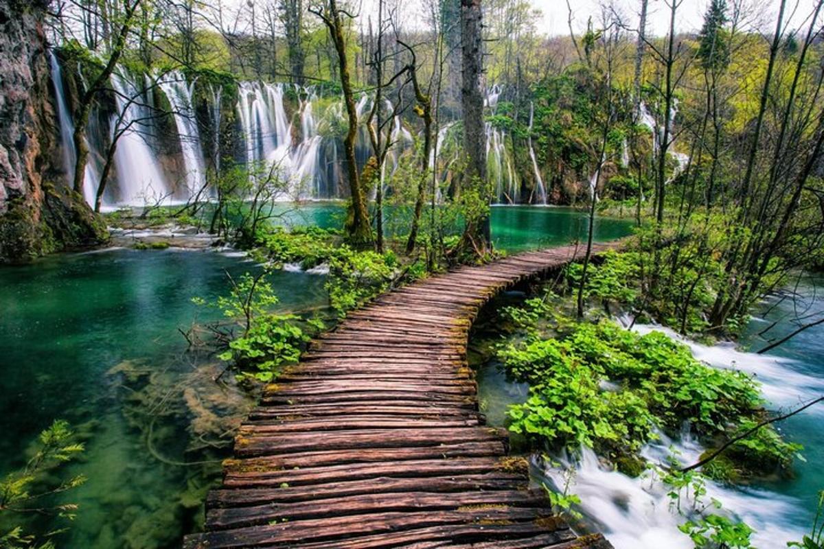 a wooden bridge over a river in front of a waterfall