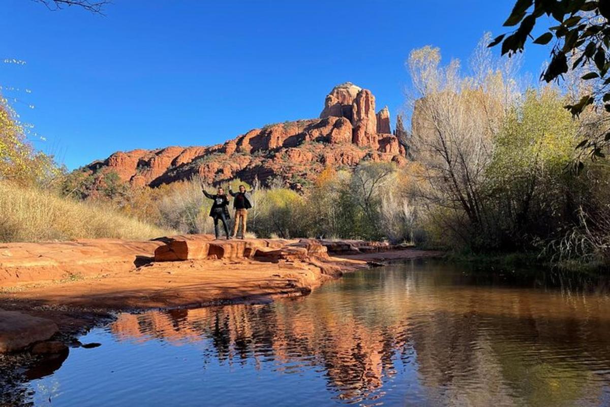 two people standing on rocks near a river with a mountain