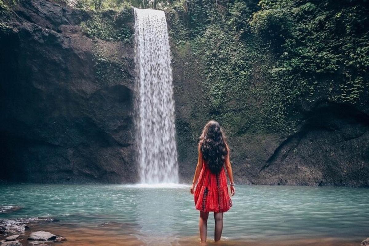 a woman standing in the water in front of a waterfall