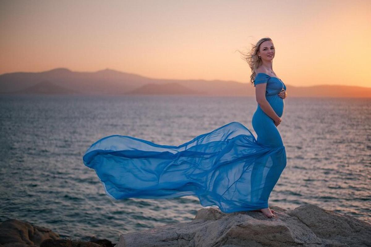 Μια γυναίκα με μπλε φόρεμα στέκεται σε έναν βράχο κοντά στον ωκεανό