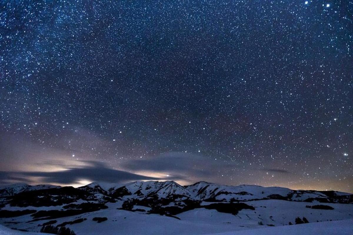 um céu noturno cheio de estrelas com montanhas na neve