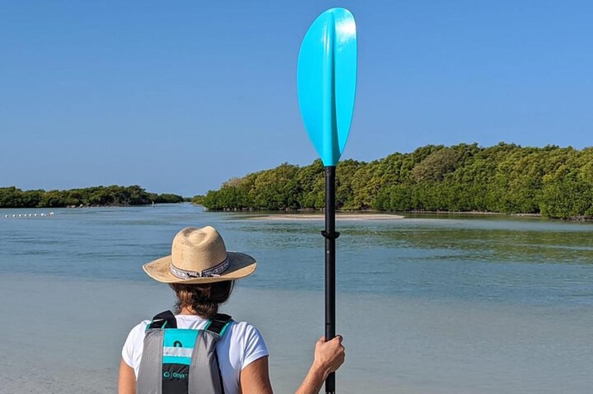 oseba s klobukom, ki drži veslo na plaži