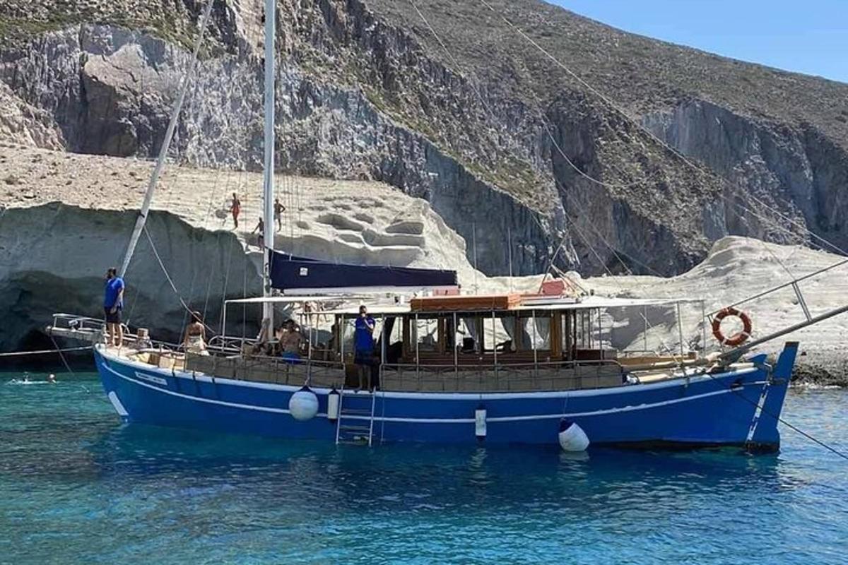 a blue boat in the water next to a cliff