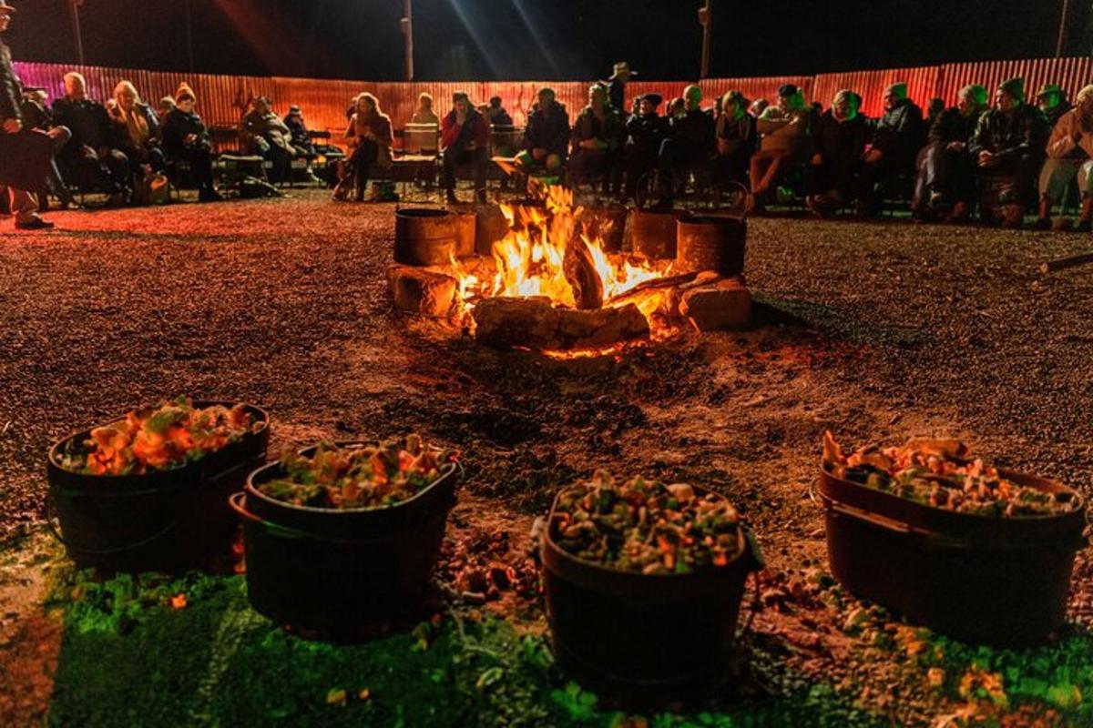 a fire pit with pots of food and a crowd of people
