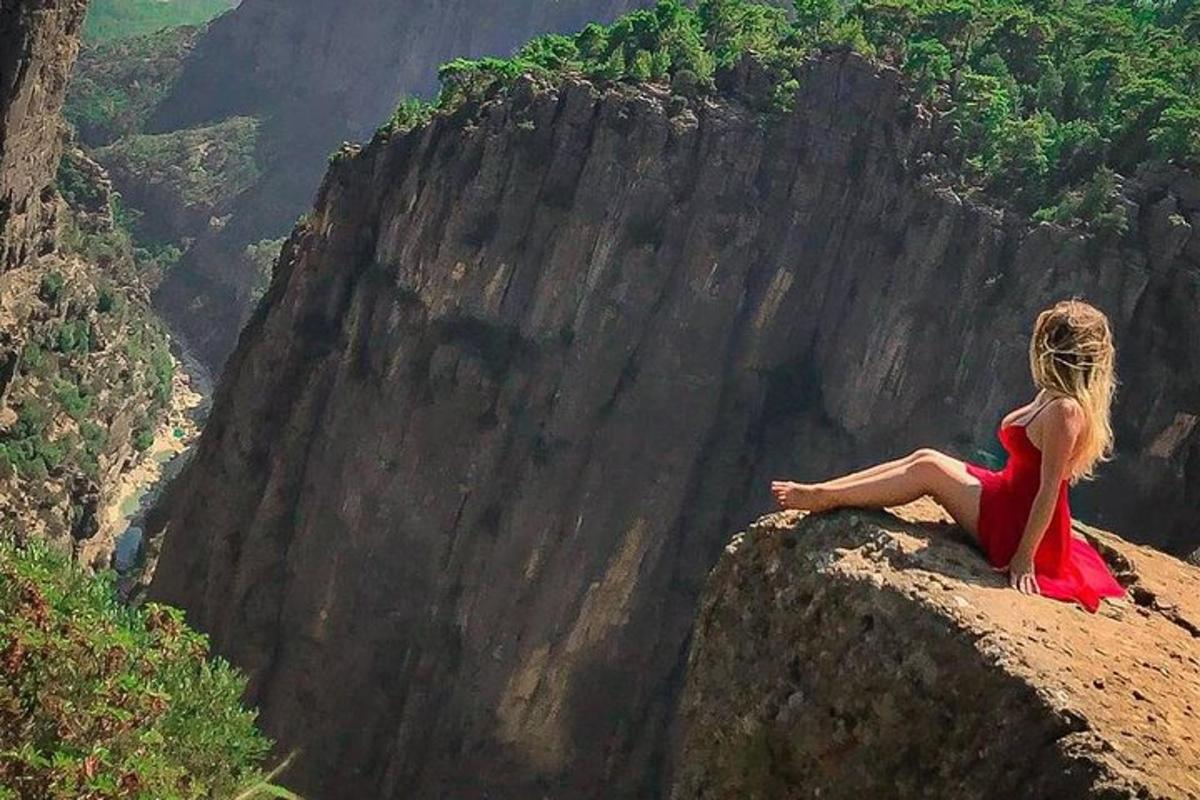 una donna in un vestito rosso seduta in cima a una scogliera