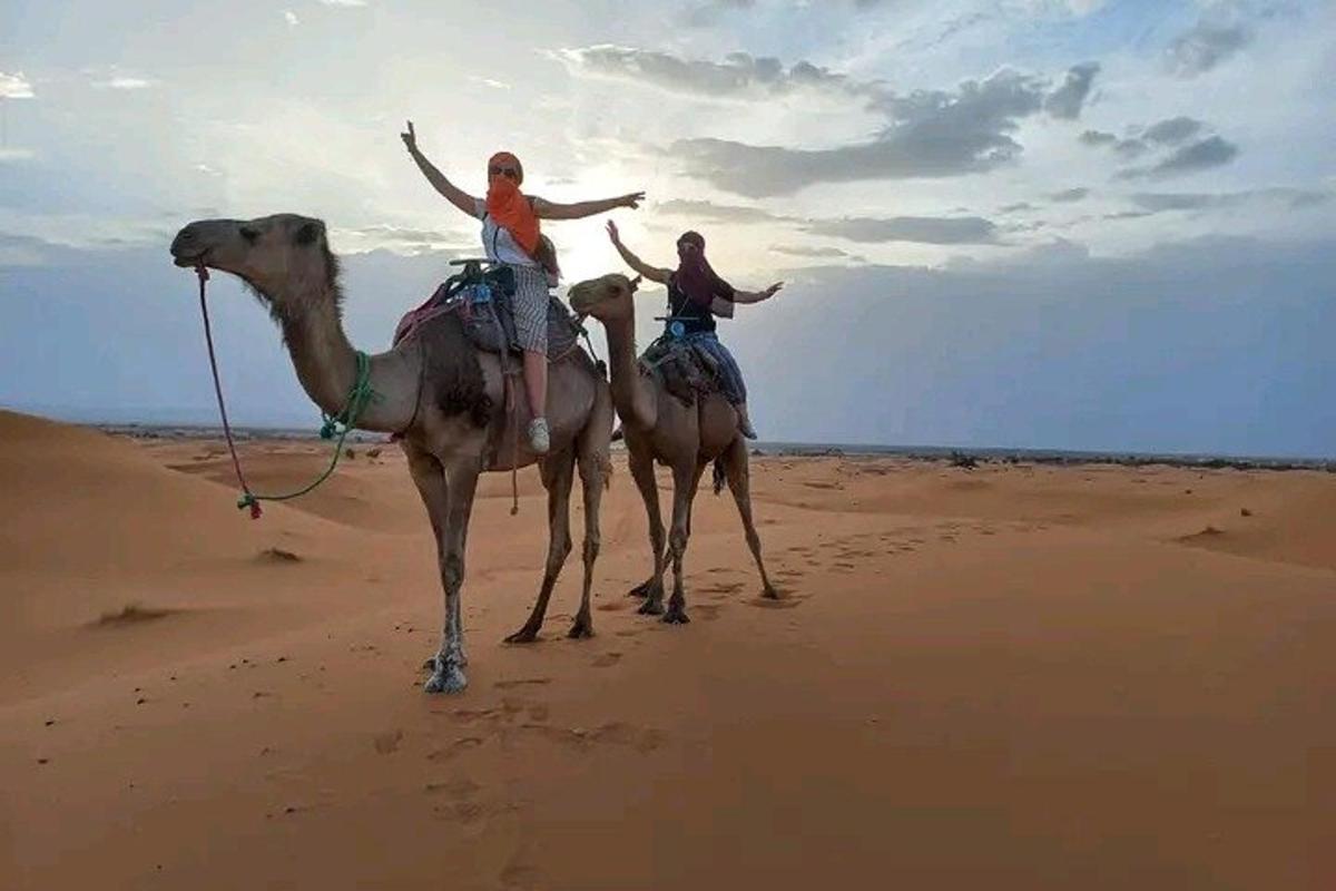 due persone a cavallo sui dorso dei cammelli nel deserto