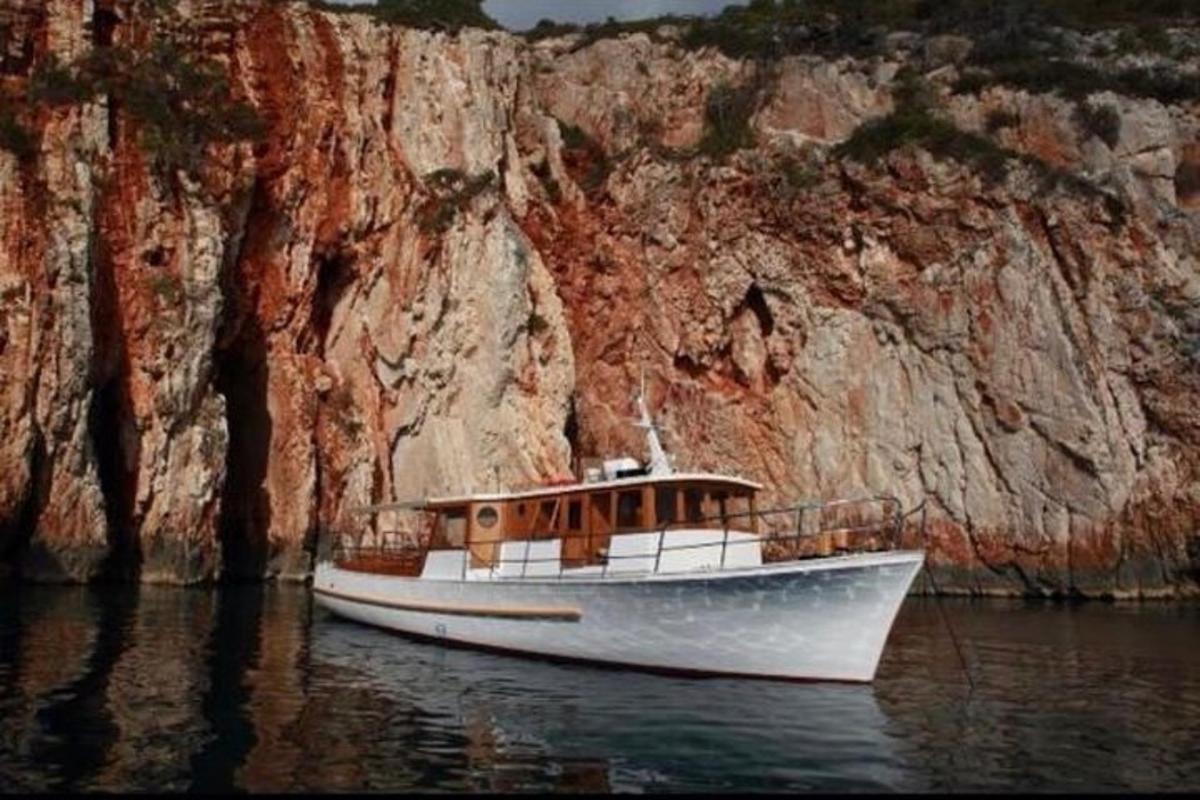 a white boat in the water next to a cliff