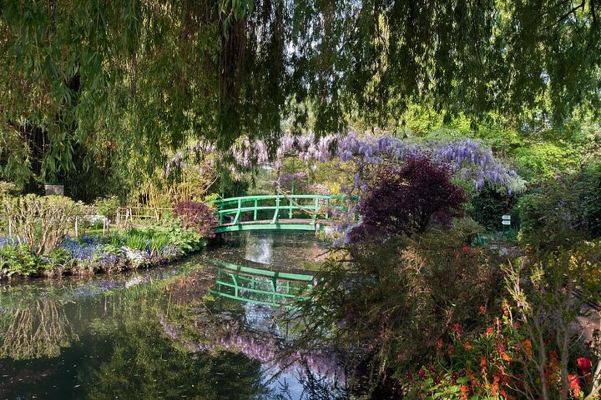 en grøn bro over en flod med lilla blomster