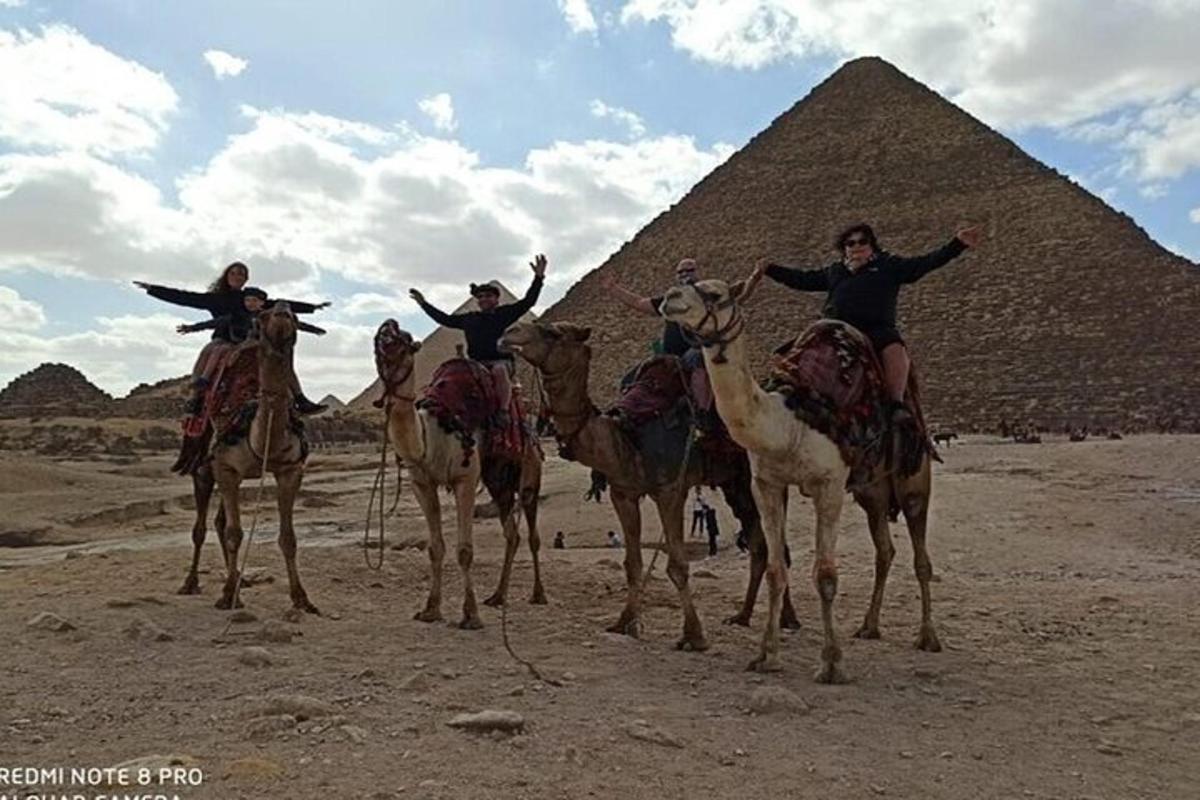 skupina ľudí na ťavách pred pyramídami