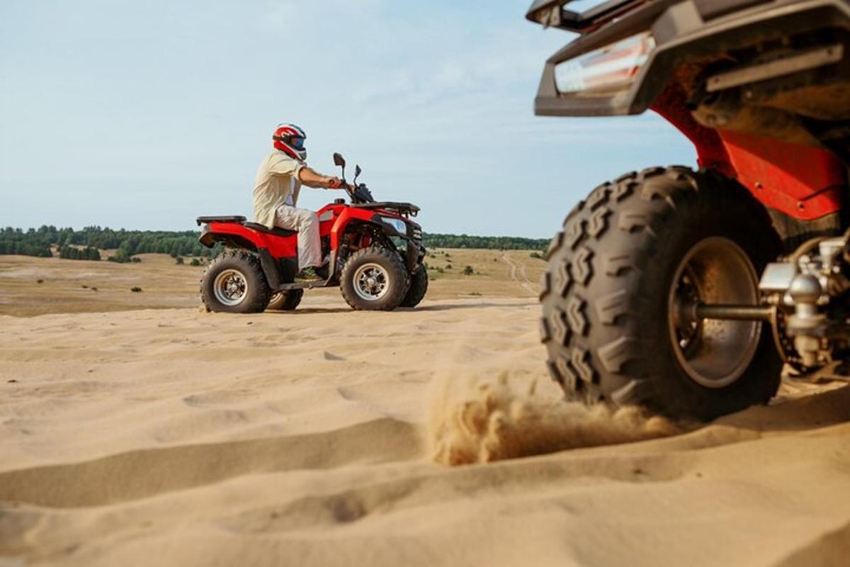 seorang lelaki menunggang basikal quad merah di dalam pasir