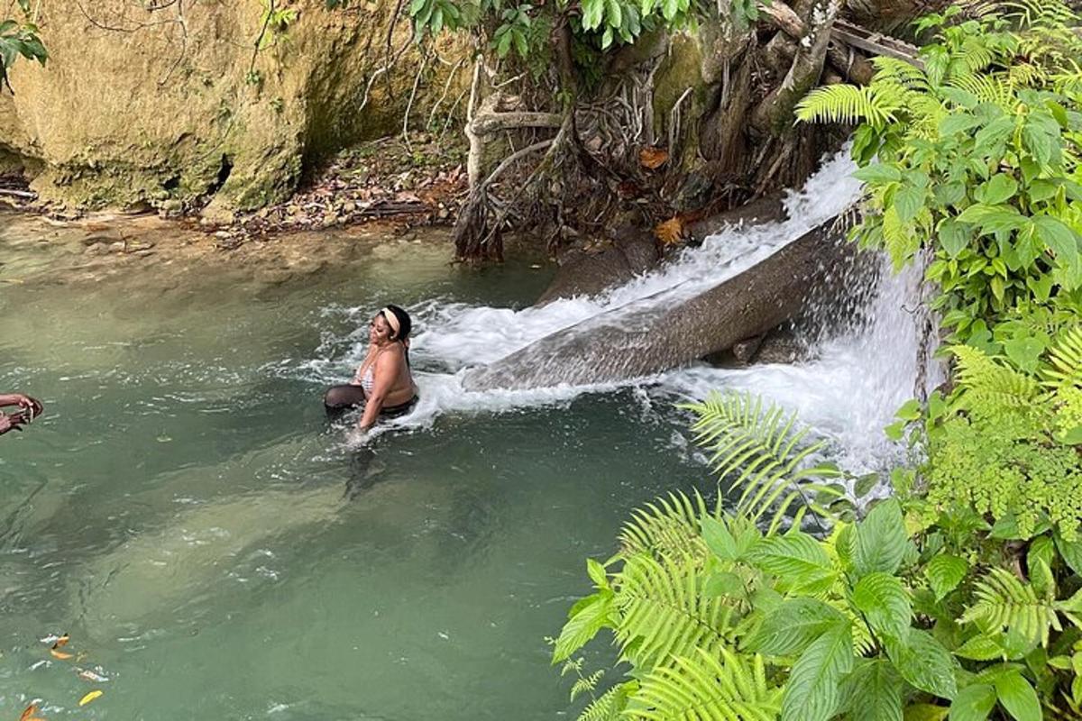 seorang wanita sedang duduk di dalam air di sebelah air terjun