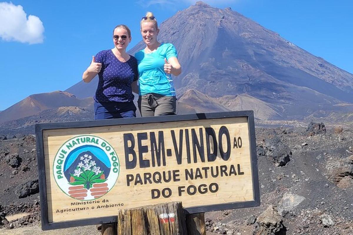 two people standing on top of a sign in front of a mountain