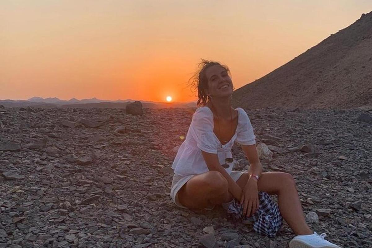 a woman sitting on the ground with the sunset in the background